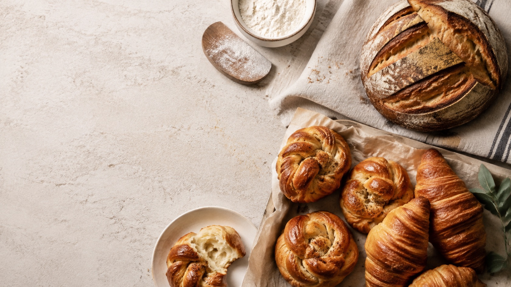 Surdejsbrød, kanelsnegle og croissanter på et lyst nordisk bagebord
